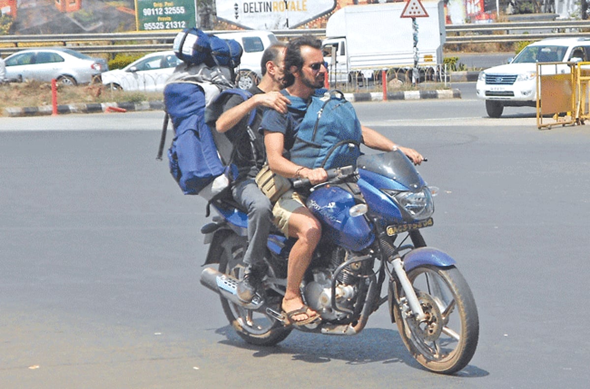 A foreign tourist relies on his friend to reach him to Dabolim airport on a hired motorcycle.