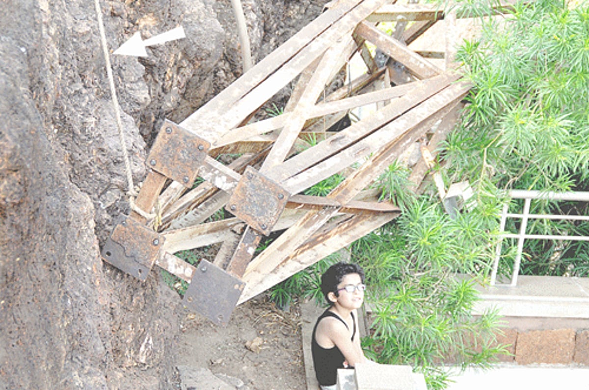 A lone tourist boy sitting below an old dismantled windmill tower precariously hanging from a nylon rope (see arrow) atop the Dona Paula jetty. The tower is yet to be removed by the authorities concerned.