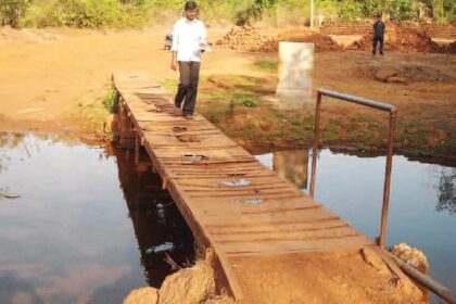A resident of Harvalem walks across a makeshift bridge, while the foundation stone for the bridge was laid years ago.