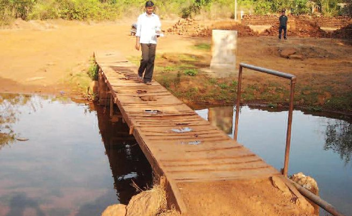 A resident of Harvalem walks across a makeshift bridge, while the foundation stone for the bridge was laid years ago.