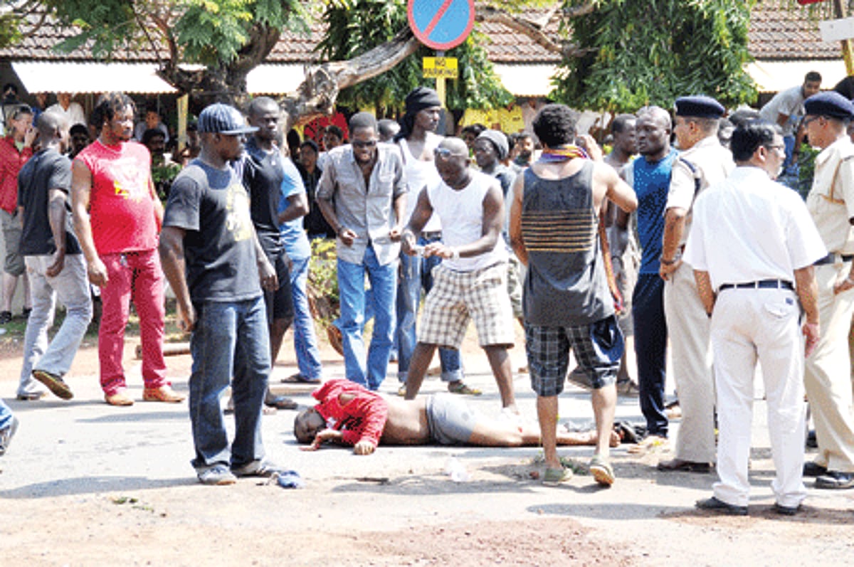 Nigerians gather around the body of Obina Poul Obirace as police look on at Porvorim.
