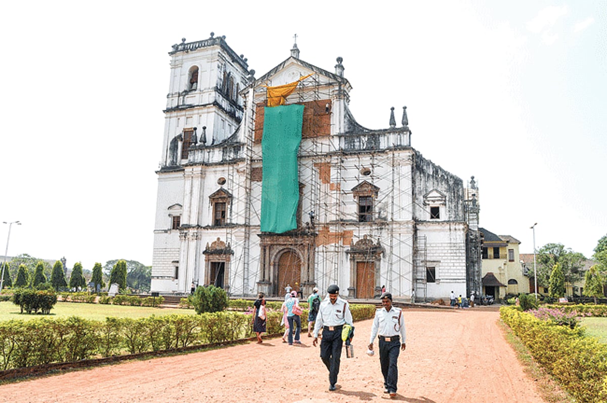 Security personal and tourist walk infront of the Se Cathedral which is under restoration with a mixture of lime, sand and mud undertaken by the Archeological Survey of India at Old Goa, on Friday