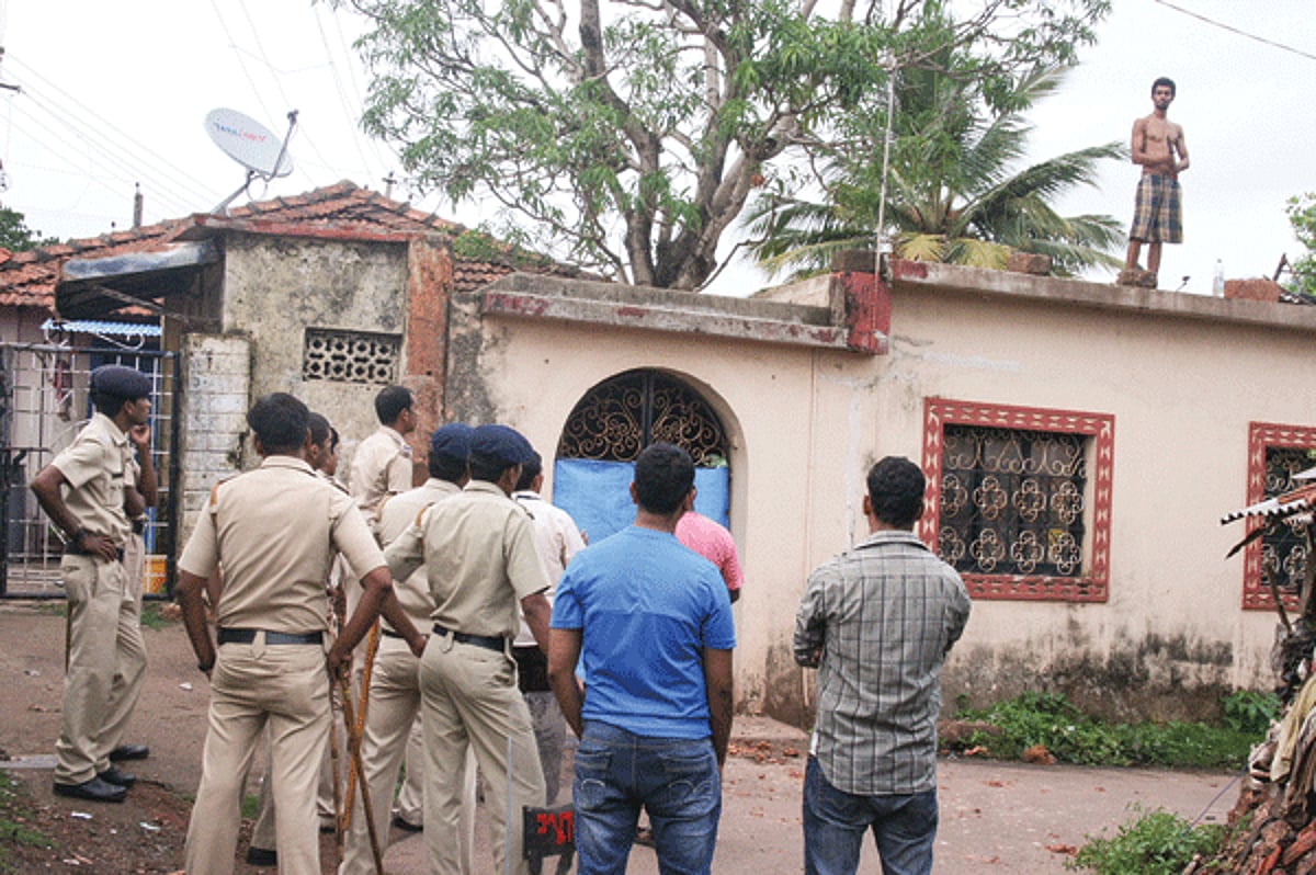 The accused on the terrace of his house armed with a knife, while police look helplessly.