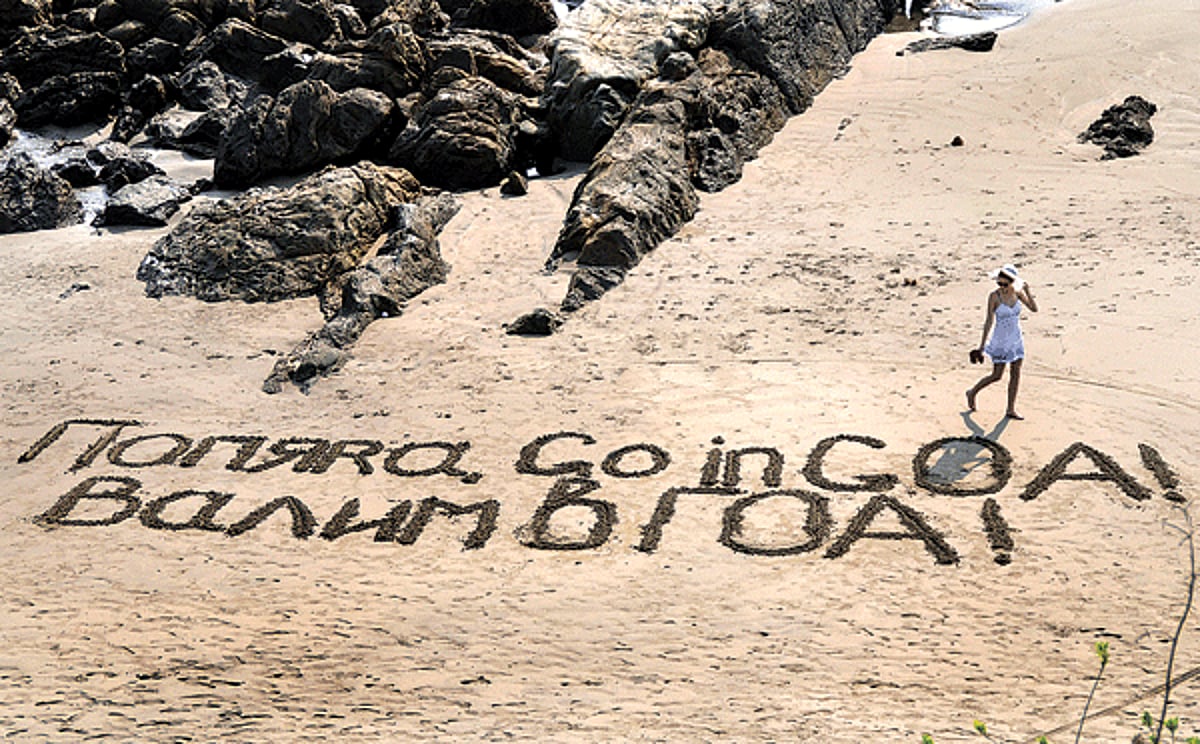 Writing on the sand: A tourist looks at the text written in Russian and English on the sands of Vagator beach