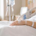 patients arm with an intravenous iv drip resting on pristine white hospital bedding photo
